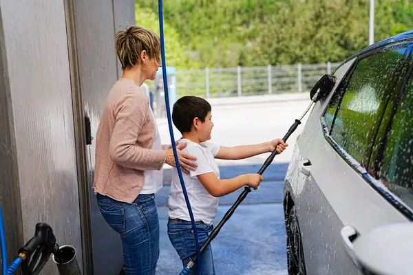 一个男孩在专心的母亲的指导下学会了洗车 图库照片