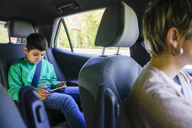 Serene car scene with child gaming and mother focused on road. clipart