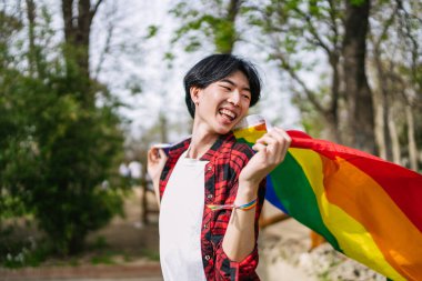 Heyecanlı Çinli gay adam gururu gökkuşağı bayrağıyla kutluyor, neşe ve enerji dolu..