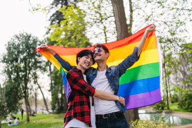 Coşkulu bir eşcinsel çift, Çinli ve Latin bir adam, özgürlüklerini ve neşelerini ifade eden parlak bir LGBT bayrağıyla kutluyor.