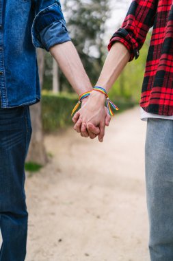 İki adam el ele tutuşuyor, LGBT bilezikleri doğal ortamda birleşmeyi sembolize ediyor..