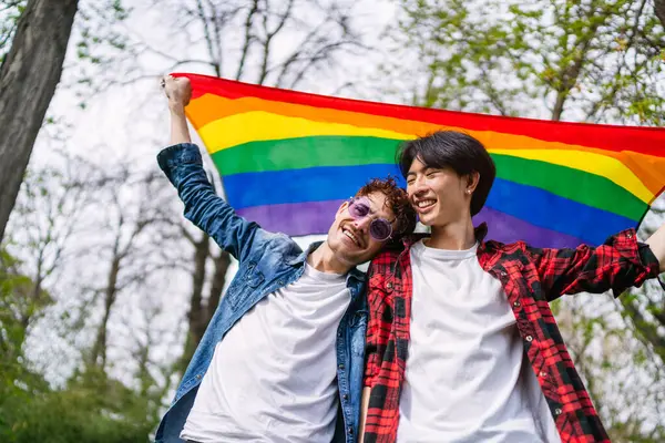 中国一对同性恋夫妇在户外高高兴兴地举着一面充满活力的Lgbt旗帜 表现出他们的爱心和自豪感 图库照片