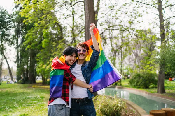 在同性恋关系中 一位中国人和拉美人在公园里与一面Lgbt旗帜欢庆 图库图片