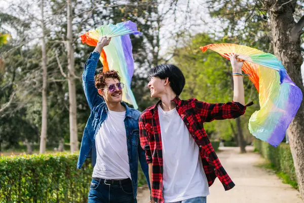 一个充满活力的日子 作为一对中国和拉美同性恋夫妇享受户外 挥动着五彩缤纷的Lgbt尾扇 图库照片