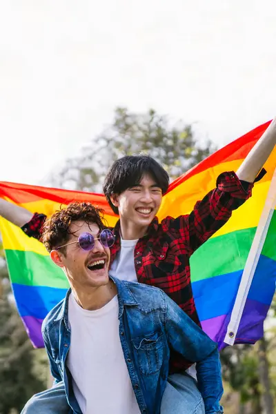 拉美和中国的同性恋情侣们共享着用Lgbt旗包裹的欢笑 享受着这一天 图库照片