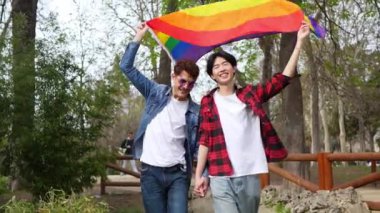 Neşeli Çinli gay çift parkta LGBT bayrağı sallıyor, enerji ve neşe saçıyor.