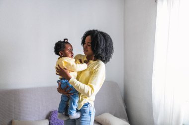 Afrikalı bir anne ağlayan bebeğini evinde kollarında rahatlatır, şefkatli ve şefkatli bir an yaratır..