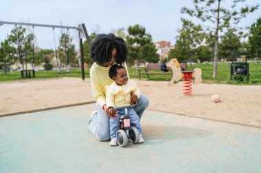 Bir kadın ve bir çocuk parkta oyuncak bir arabada oturuyorlar. Kadın çocuğun elini tutuyor.