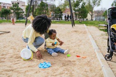 Parkta bir kadın bir çocukla oynuyor. Çocuk bir oyuncak tutuyor ve kadın onunla oynamak için diz çöküyor. Sahne neşeli ve neşeli, kadınlayken.