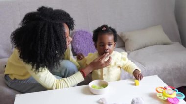 Genç Afrikalı anne bebek üzümlerini besliyor, onlar da mutlu bir şekilde alkışlıyor, 4K yavaş çekimde hassas ve neşeli bir an yaratıyorlar..