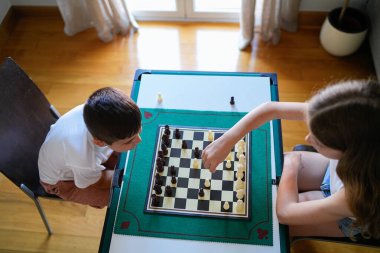 Bir kız ve erkek satranç oynuyorlar. Kız yerde otururken oğlan bir sandalyede oturuyor.