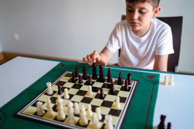 Bir çocuk satranç oynuyor. Tahtaya odaklanmış ve bir parçaya uzanıyor.