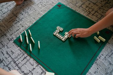 Bir kişi, bir arkadaşıyla domino oynuyor. Oyun tahtası yeşil ve üzerinde beyaz 