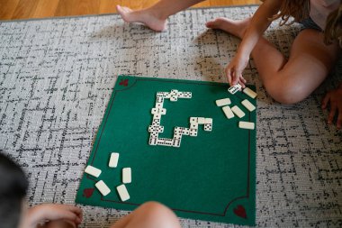 Domino oynayan iki kişi. Oyunculardan biri fayansa uzanıyor.