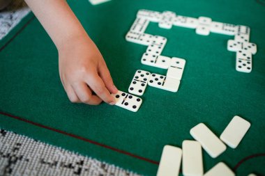 Bir çocuk domino taşlarıyla oynuyor. Çocuk yeşil bir fayansın üstüne beyaz bir domino taşı koyuyor.