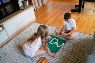 Yeşil bir tahtada domino oynayan iki çocuk. Sahne neşeli ve şen şakrak
