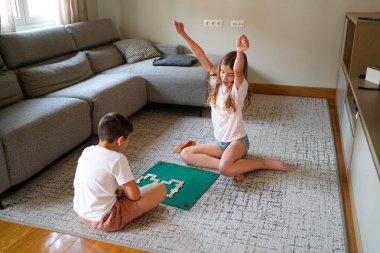 İki çocuk yeşil bir hasırda domino oynuyor. Çocuklardan biri şort giyiyor.