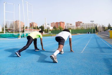 İki Afrikalı atletizm pistinin başlangıç çizgisinde koşmaya hazır bekliyor. Manzara arkadan ve gerilim var gibi görünüyor.