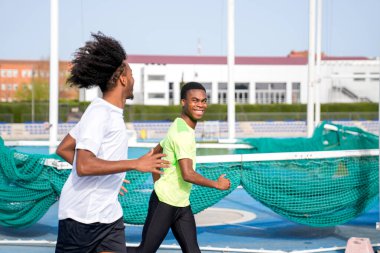 İki Afrikalı bir adam pistte koşuyor, biri yeşil tişörtlü. Sahne enerjik ve aktiftir