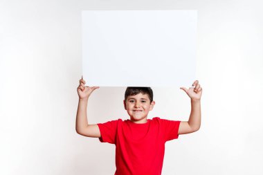 Genç bir çocuk elinde beyaz bir işaret tutuyor. Çocuk kırmızı gömlek ve mavi kot pantolon giyiyor.