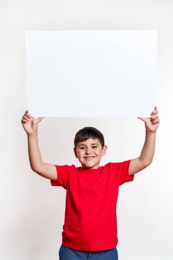 Genç bir çocuk elinde beyaz bir işaret tutuyor. Çocuk kırmızı gömlek ve mavi kot pantolon giyiyor.