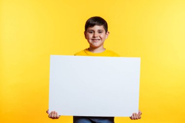 Genç bir çocuk yüzünde bir gülümsemeyle beyaz bir tahta tutuyor. Olumluluk ve coşku kavramı, çocuk beyaz tahta konusunda heyecanlı görünüyor.