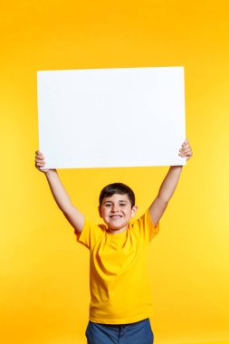 Genç bir çocuk elinde boş bir tabela tutuyor. Çocuk gülümsüyor ve mutlu. Tabela beyaz ve üzerinde yazı yok. Olumlu ve heyecan kavramı