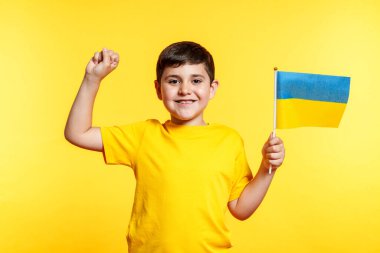 Genç bir çocuk Ukrayna bayrağı tutuyor ve gülümsüyor. Çocuk kutlama yapıyor..