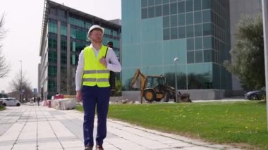 Yansıtıcı yelek giymiş kızıl saçlı bir mimar, bir inşaat alanında makineli tüfeği tutarken gülümsüyor..