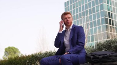 Mavi takım elbiseli genç, kızıl saçlı bir işadamı, dışarıda oturan bir telefon görüşmesinde iyi haberler aldıktan sonra yumruğunu havaya kaldırarak kutlama yapıyor..