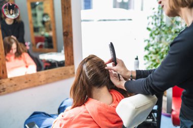 Bir kuaför modern bir kuaförde müşterinin saçını dikkatlice tarar. Odaklanma amacı profesyonel tekniktir. Ayrıntılı saç bakımı kavramı.