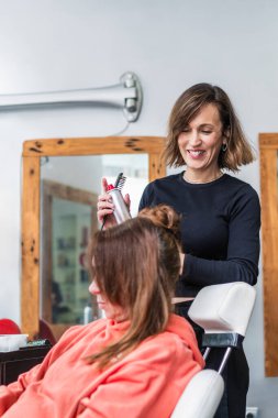 Bir kuaför, bir müşterinin saçını bir salonda taramak için sprey ve tarak kullanır. Sahne profesyonel bakım ve tekniği vurguluyor. Ayrıntılı saç bakımı kavramı.