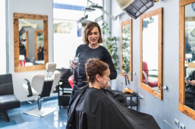 Bir kuaför, modern bir kuaförde müşterinin saçına büyük aynalar püskürtür. Profesyonel saç bakım ve tasarım kavramı.