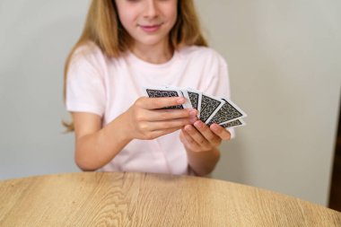 Bir kız iskambil destesiyle kağıt oynuyor. Gülümsüyor ve kartları elinde tutuyor.