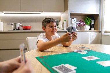 Bir çocuk bir insanla iskambil oynuyor. Çocuk elinde bir kart tutuyor.