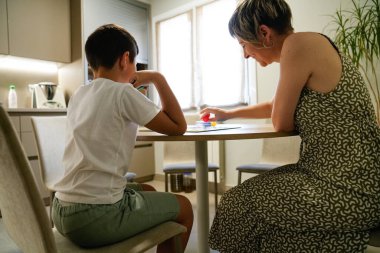Bir anne ve oğul mutfakta Parcheesi oynarken gülümserler. Sahne onların neşesini yakalar ve parlak ortam pozitif atmosfere katar. Neşeli etkileşim kavramı.