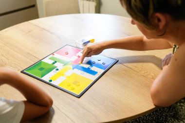 Bir anne ve oğlu Parcheesi yönetim kurulunda strateji geliştiriyor, ikisi de oyuna odaklanmış. Renkli kurul ve etkileşimleri düşünceli ve ilgi çekici oyunun altını çiziyor. Stratejik bağ kavramı.