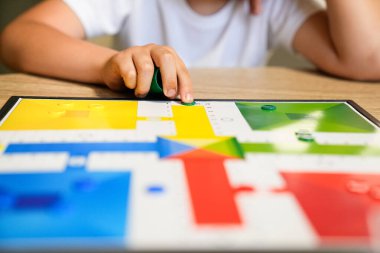 Bir çocuk oyuna konsantre olmak için Parcheesi tahtasında bir parça hareket ettiriyor. Renkli tahta ve çocuğun eli odak noktaları, nişanlı oyunun altını çiziyor. Odaklanmış oyun kavramı.