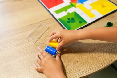 Bir çocuğun Parcheesi 'nin parçalarını masaya dizerken çekilmiş yakın plan fotoğrafı. Maç için hazır. Renkli pano görünür, hazırlık aşamasını vurguluyor. Oyuna hazır olma kavramı.