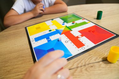 Genç bir çocuk, annesi bir parça taşırken bir masa oyununa konsantre olur. Stratejik düşünme ve aile bağı kavramı.