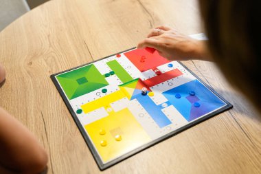 Bir anne oğluyla oynarken Parcheesi tahtasında bir parça hareket ettirir. Renkli kurul ve onların odaklanmış bağlılıkları stratejik oyunu vurguluyor. Bağlı strateji kavramı.