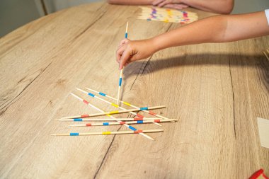 Bir çocuğun eli konsantrasyon odaklı bir aile oyununda sopayı ustalıkla çıkarır, odaklanmayı ve hassasiyeti gösterir. Stratejik düşünme ve el becerisi kavramı.
