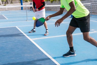 Pickleball oyuncularından oluşan çok ırklı bir grubun yakın çekimi açık hava sahasında oynanan bir maçta topa vurmaya odaklandı. Odaklanma ve takım çalışması kavramı.