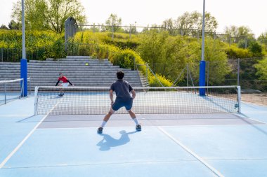 İki oyuncu, parlak mavi bir picleball sahasında rekabetçi bir mitinge katılıyor. Spor alanında rekabet ve strateji kavramı.