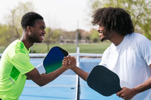 İki Afrikalı oyuncu güldü ve Pickleball sahasında ağın üzerinden el sıkıştı. Sportmenlik kavramı, Afrika etnik kökeni ve dostluk..