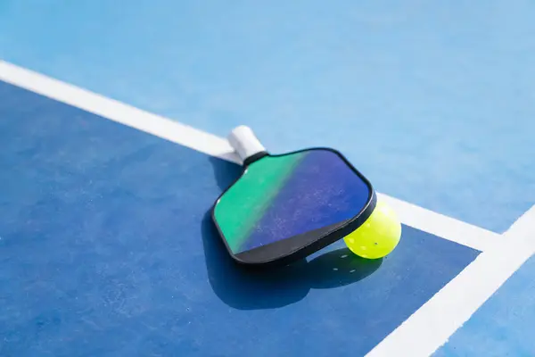 Pickleball raketi ve topunun yakın plan çekimi yan çizgide mavi bir kortta dinleniyor. Spor malzemesi kavramı.