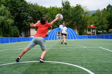 Genç bir çocuk, annesi tarafından güneşli bir arazide atılan bir futbol topunu yakalıyor. Aile sporu ve takım çalışması kavramı.