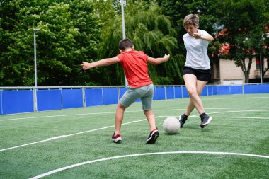 Bir anne futbol topunun kontrolü için oğluyla yarışır. Aile eğlencesi ve spor rekabeti kavramı.