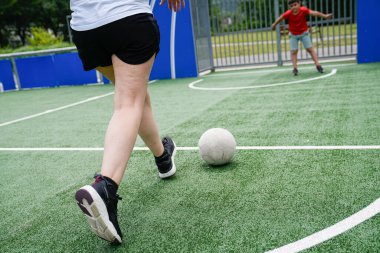 Anne ve oğlu top sürme ve defansa odaklanarak bir futbol maçında yarışıyorlar. Aile bağları ve spor yoluyla öğrenme kavramı.