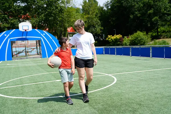 Bir anne ve oğlu futbol sahasında kol kola yürür. Oğlu da elinde top tutardı. Aile anlarını paylaşılan faaliyetlerle besleme kavramı.